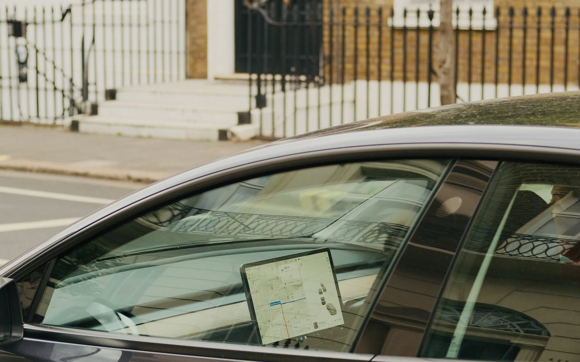 Grey Tesla Model 3 parked on a London street in front of a Georgian terrace with black railings, its touchscreen showing a map